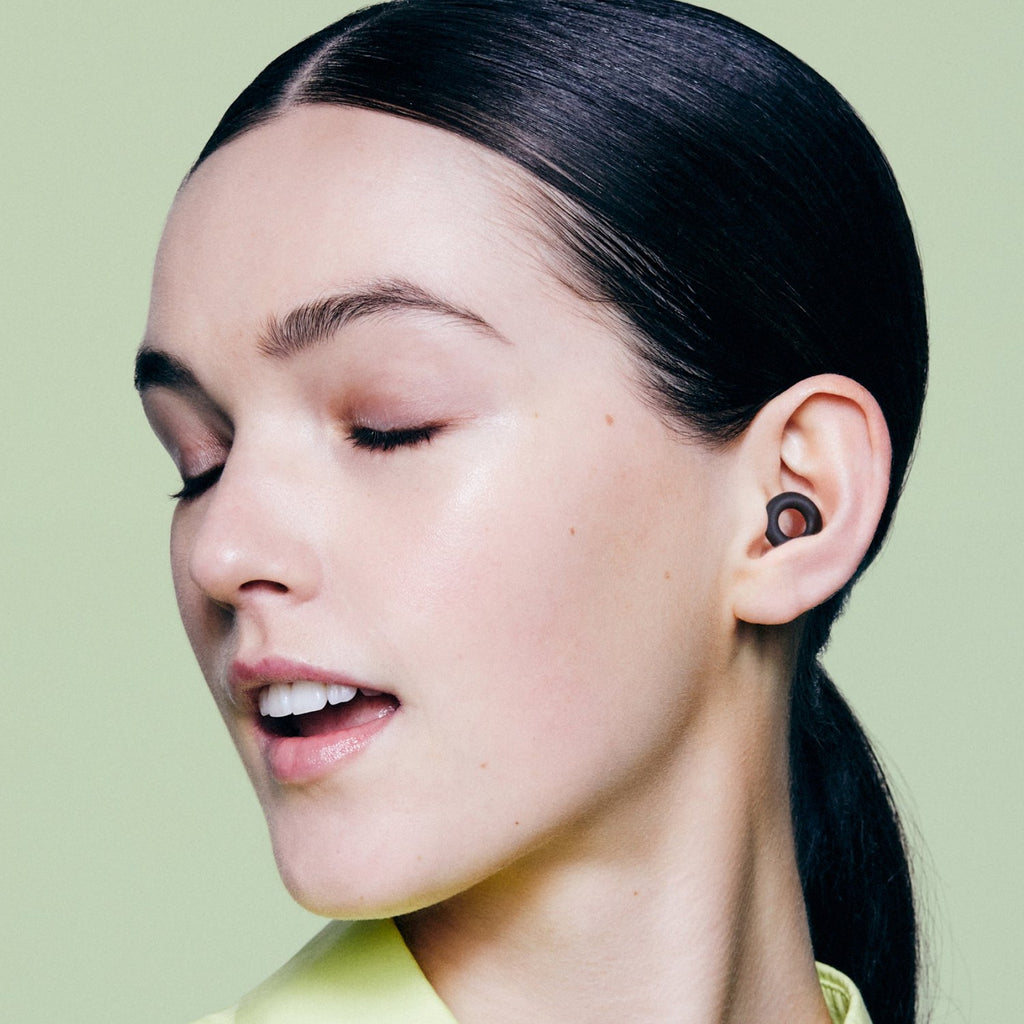 Woman with her eyes closed wearing a Black PLUGS earplug
