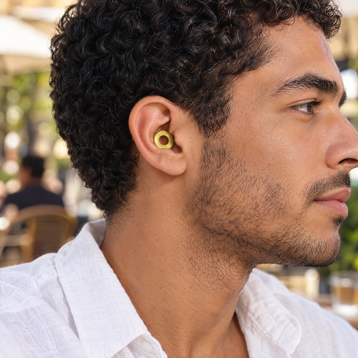 Man with curly hair wearing a Gold PLUGS earplug, shown from the side
