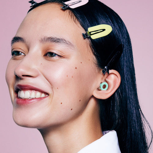 Smiling woman wearing a Mint PLUGS earplug, the ring sitting flat in her outer ear