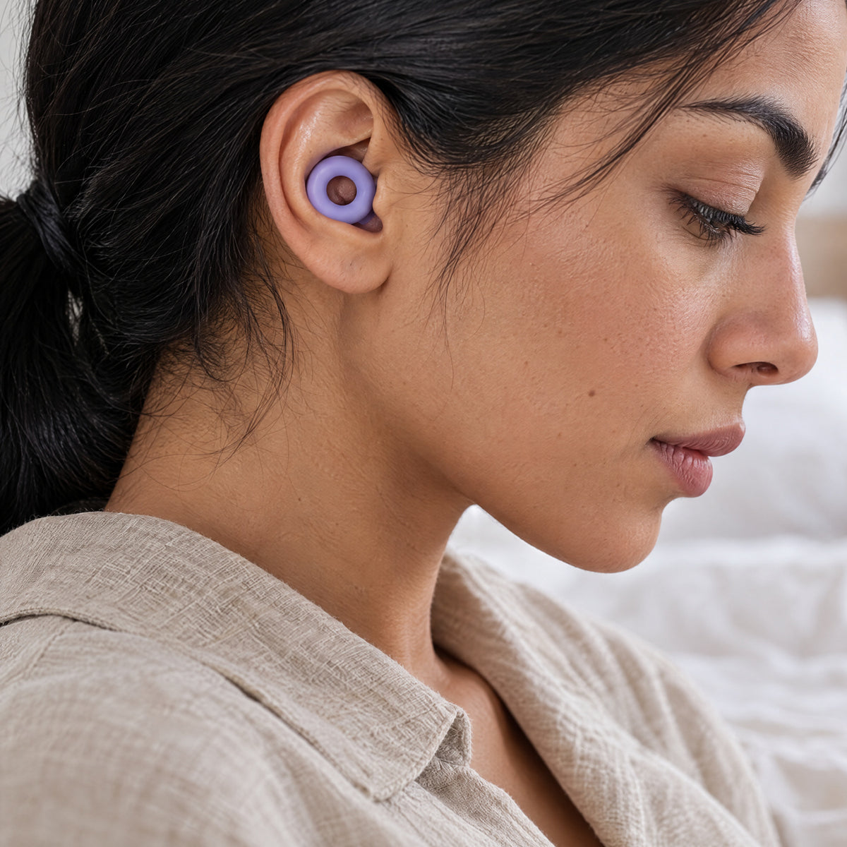 Woman looking down, wearing a Violet PLUGS earplug, the ring sitting flat in her outer ear