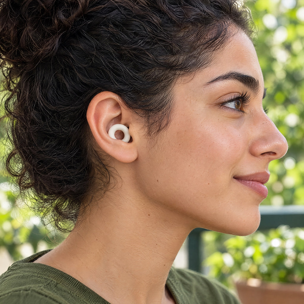 Smiling woman with curly hair wearing a White PLUGS earplug, shown from the side